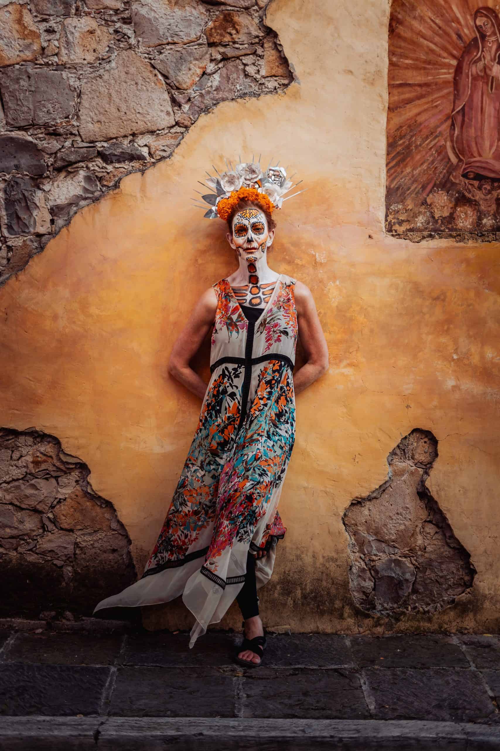 Artist Jacqueline von Edelberg wearing colorful skeleton face paint and festive dress celebrating San Miguel de Allende's Day of the Dead, honoring Mexican traditions.
