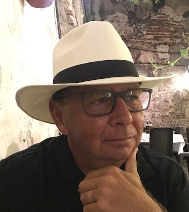 Elegant man wearing a white fedora hat with a black band and glasses, enjoying a relaxed moment in San Miguel de Allende, Mexico.